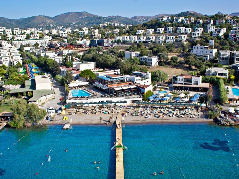 Vista al mar de un resort hotelero con piscinas, playa y montañas al fondo.