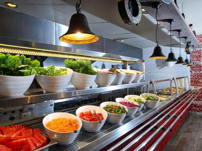 Buffet con varias ensaladas frescas e ingredientes en tazones blancos bajo lámparas colgantes.