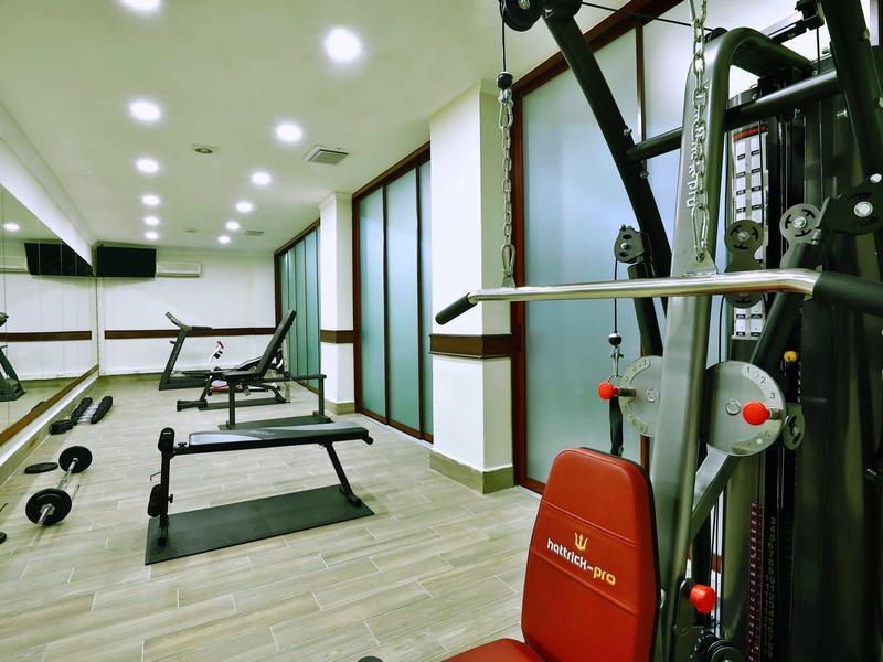 Gimnasio moderno con máquinas de ejercicio, banco de pesas y suelo de madera clara.