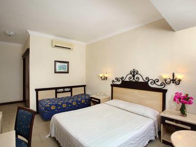 Hotelzimmer mit Doppelbett, Sofa, Nachttischen und Blumen auf dem Tisch.