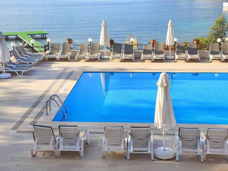 Piscine avec transats et parasols au bord calme d'un lac d'hôtel.