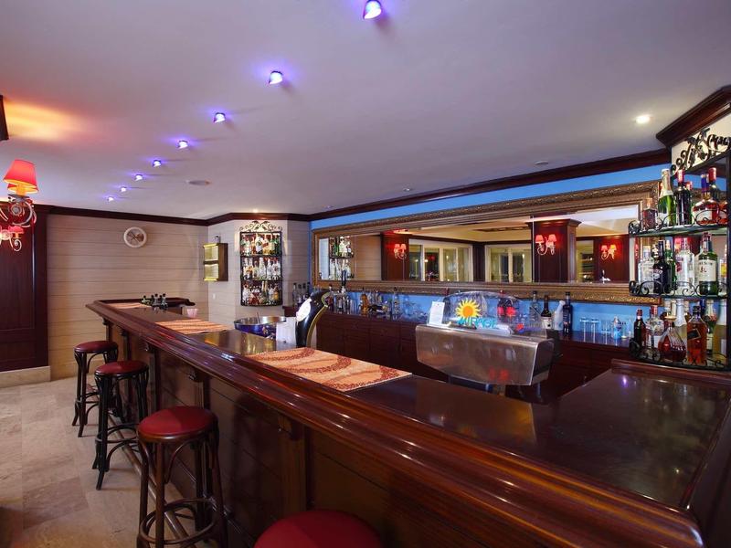 Bar élégante avec comptoir en bois, tabourets rouges et étagère éclairée avec spiritueux.