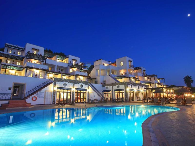 Luxuriöses weißes Hotel mit beleuchtetem Pool und klarer blauer Abendhimmel mit Mond.