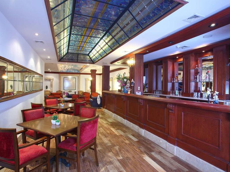 Elegante Bar mit Holzverkleidung, roten Sesseln, Holztischen und farbigem Glasdachfenster.