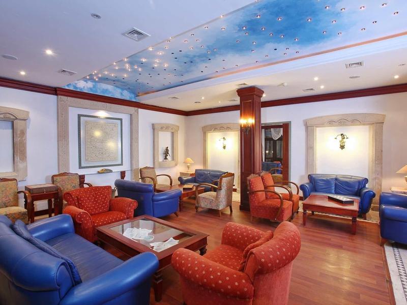 Wohnzimmer mit blauen und roten Sesseln, Holzboden, weißen Wänden und Himmelsdecke mit Wolkenmotiv.