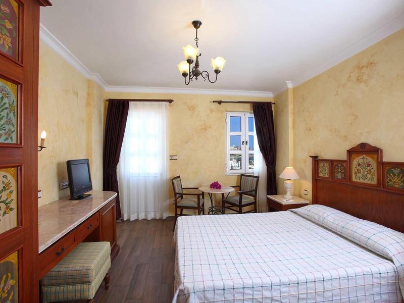 Gemütliches Schlafzimmer mit Doppelbett, Holzmöbeln, Tisch mit Stühlen und hellem Fensterlicht.