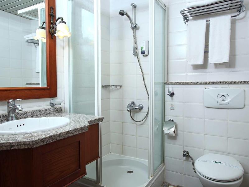 Helle kleine Bad mit runder Dusche, Toilette, Waschbecken und Handtüchern an weiß gefliesten Wänden.