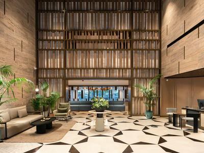 Hall d'hôtel moderne avec murs en pierre, grandes plantes et sols géométriques.