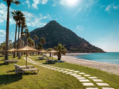 Strandresort mit Liegestühlen, Palmen und einem Berg im Hintergrund unter blauem Himmel.