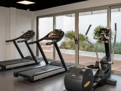 Ein moderner Fitnessraum mit Laufbändern und einem Ellipsentrainer vor großen Fenstern.