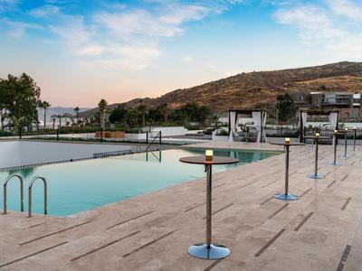 Piscine extérieure avec terrasse en pierre et vue sur colline sous un ciel bleu.