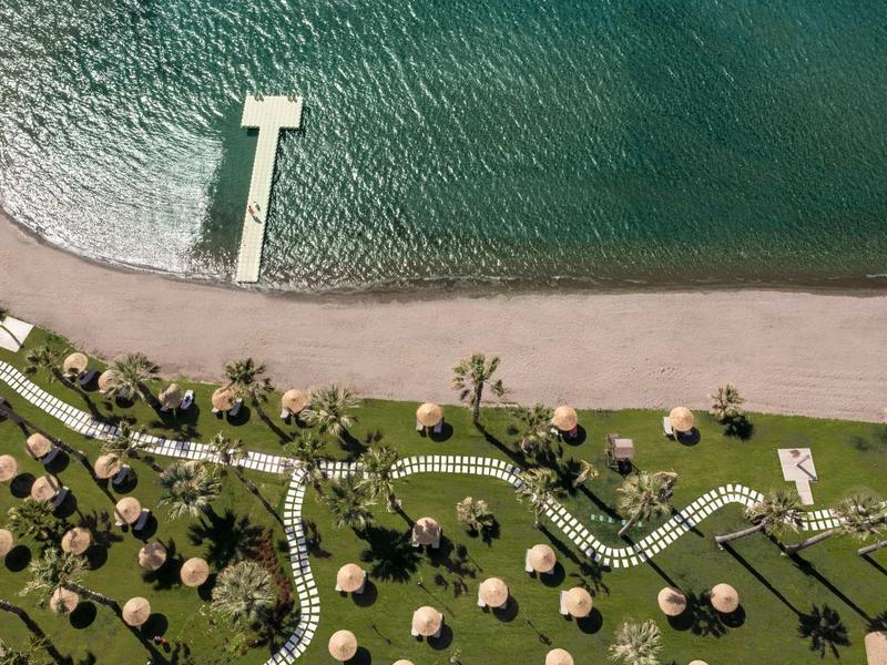 Vue aérienne d'une plage avec une jetée et des parasols sur pelouse verte.