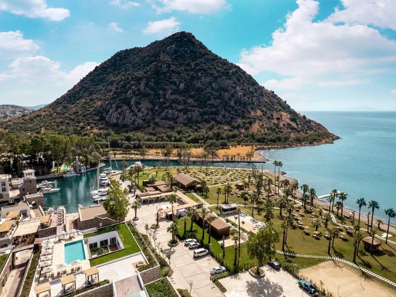 Vue côtière d'un hôtel avec jardin, plage et grande montagne en arrière-plan.