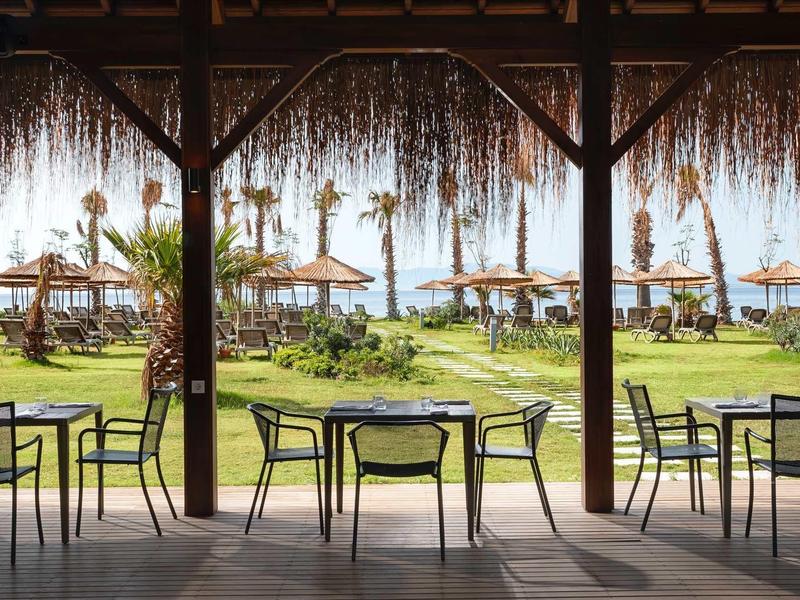 Terrasse ombragée avec tables et chaises, vue sur jardin et parasols au bord de l'eau.