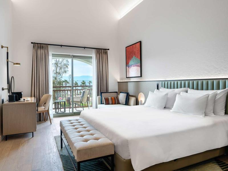 Chambre d'hôtel moderne avec lit king-size, balcon et vue sur la mer.