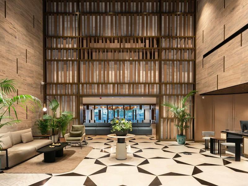 Hall d'hôtel moderne avec murs en pierre, grandes plantes et sols géométriques.