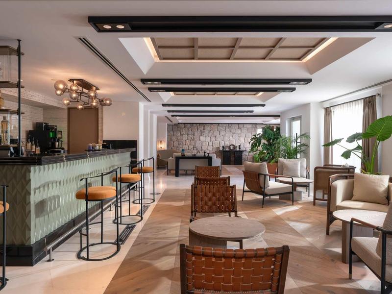 Salon lumineux d'hôtel avec bar, sièges en cuir et grandes fenêtres.