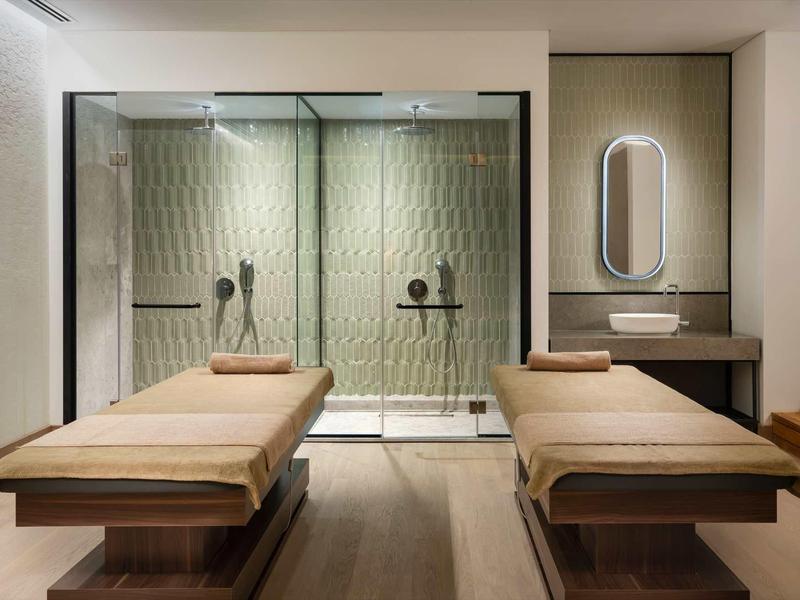 Salle de massage moderne avec deux tables et douche en verre.