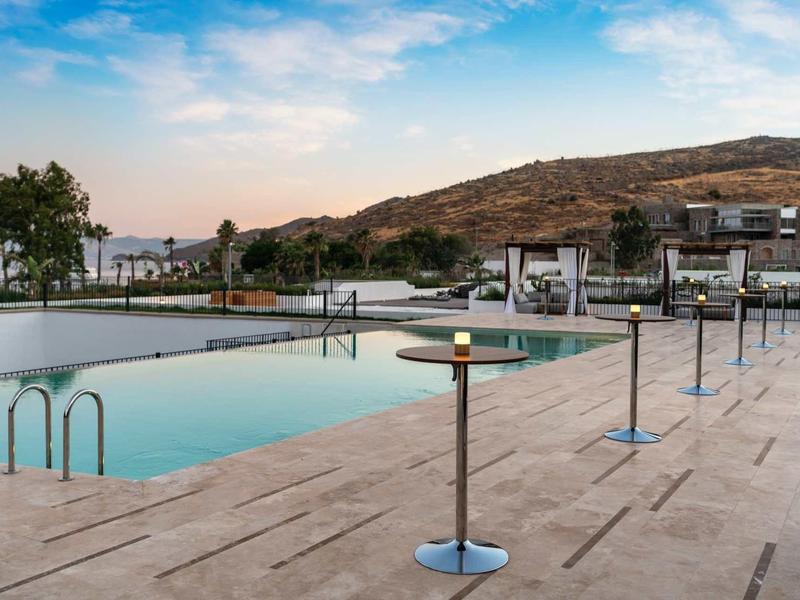 Piscine extérieure avec terrasse en pierre et vue sur colline sous un ciel bleu.