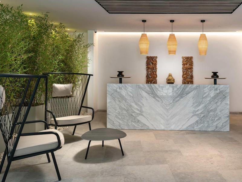 Réception d'hôtel moderne avec comptoir en marbre et sièges confortables près d’un mur végétal.