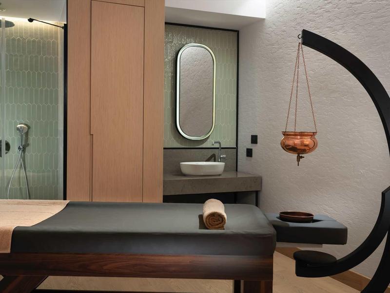 Salle de massage élégante avec table, miroir ovale, douche et décor moderne.