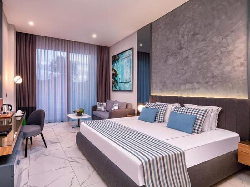 Habitación de hotel moderna con cama doble, área de estar, escritorio y grandes ventanas con cortinas.