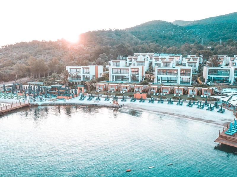 Un resort junto al agua con piscinas, playas y colinas al fondo al atardecer.