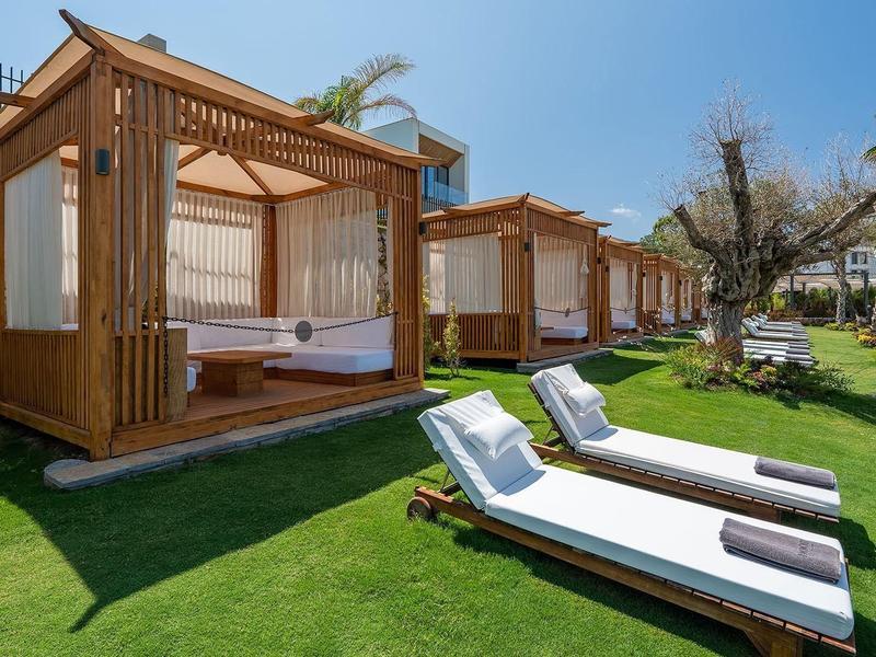 Cabañas modernas de madera con cortinas blancas sobre césped verde bajo un cielo despejado en el hotel.