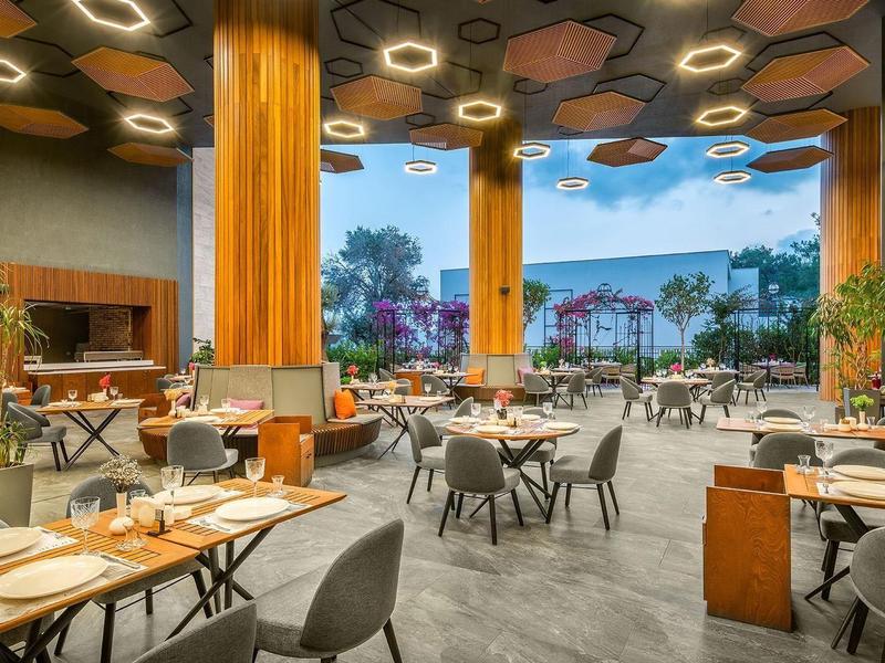 Área de restaurante de hotel moderno con mesas puestas y vista a palmeras.