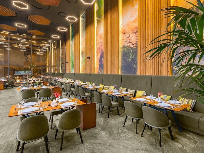 Restaurante moderno con techos altos, paneles de madera y mesas elegantemente preparadas.