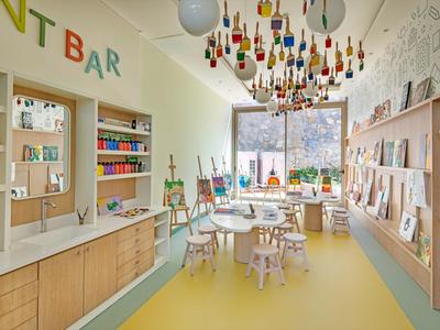 Bright art room with children's furniture, easels, and colorful bottles hanging from the ceiling.