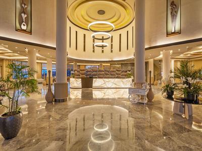 Large hotel lobby with round reception desk, marble floor, and modern decorative elements.
