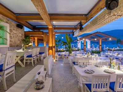 Open, stylishly decorated outdoor restaurant area with white tables and chairs at dusk.