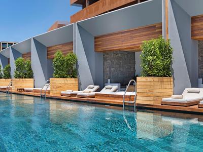 Modern hotel pool with sun loungers and private niches, surrounded by wood and plants.