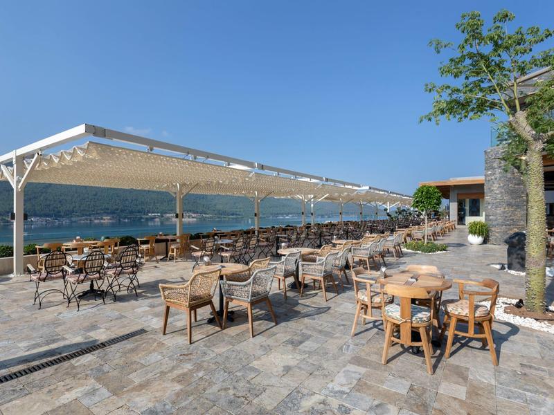 Large terrace with many tables and chairs under a blue sky overlooking the sea.