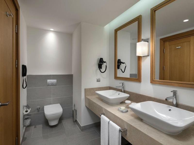 Modern hotel bathroom with two sinks, large mirrors, and a toilet.
