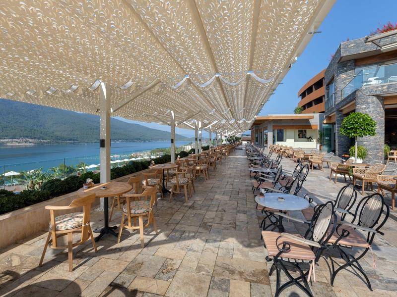 Large outdoor terrace with tables and chairs next to a hotel with mountain and lake views.