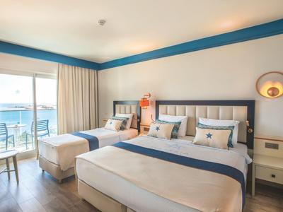 Hell eingerichtetes Hotelzimmer mit Doppelbett, Sofa, Balkon und Meerblick.