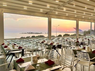 Offenes Restaurant mit Meerblick bei Sonnenuntergang, gedeckte Tische und weiße Stühle.