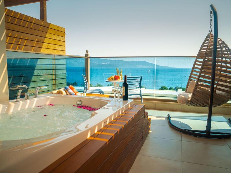 Hotelová terasa s vířivkou, lehátkem a výhledem na moře za západu slunce.