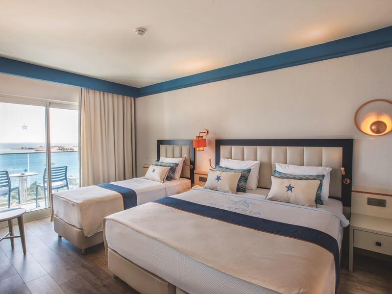 Moderní hotelový pokoj s manželskou postelí, křeslem, balkonem a výhledem na moře.