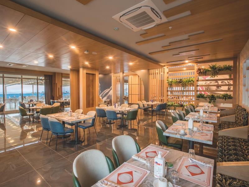 Moderní restaurace s velkými okny s výhledem na moře, prostřené stoly a pohodlné židle.