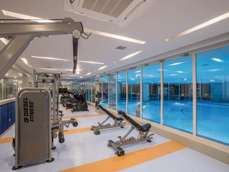 Moderní posilovna se stroji a výhledem na vnitřní bazén.