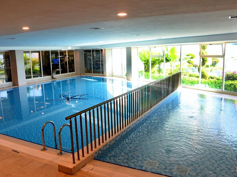 Prostorný krytý bazén s denním světlem a kovovým zábradlím mezi dvěma bazény.