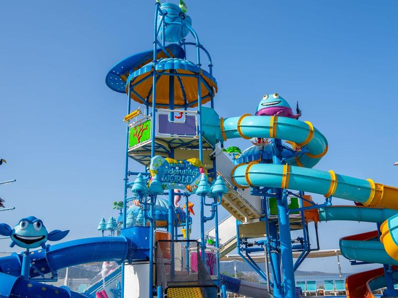 Barevná vodní herní konstrukce se skluzavkami pod jasnou modrou oblohou.