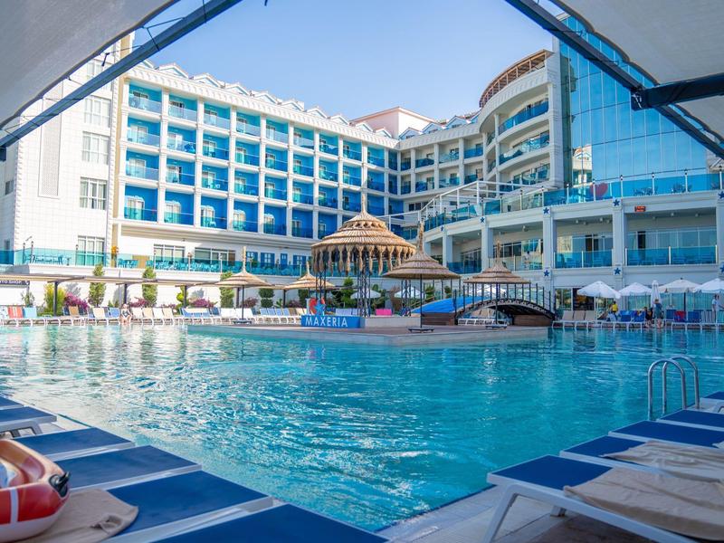 Velký moderní hotel s modrým bazénem a centrálním mostem za slunečného dne.