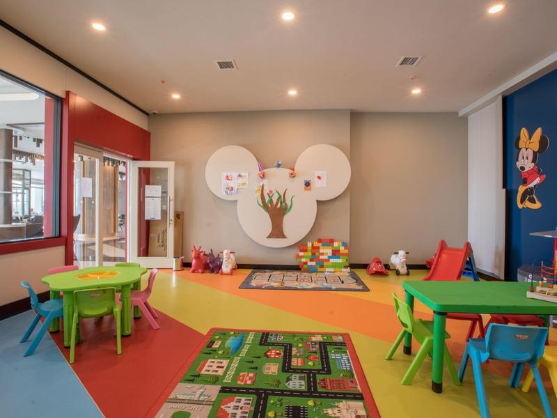 Barevná dětská herna s lavicemi, židlemi a hračkami v prosvětleném prostoru.