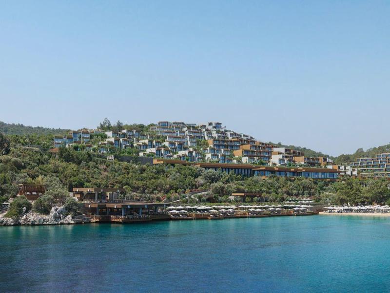 Vista de una bahía tranquila con agua azul clara y colinas verdes al fondo bajo clima soleado.