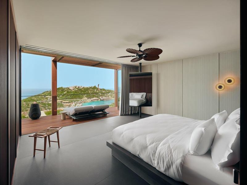 Habitación de hotel moderna con cama grande, vista abierta al mar y zona de descanso acogedora en la terraza.