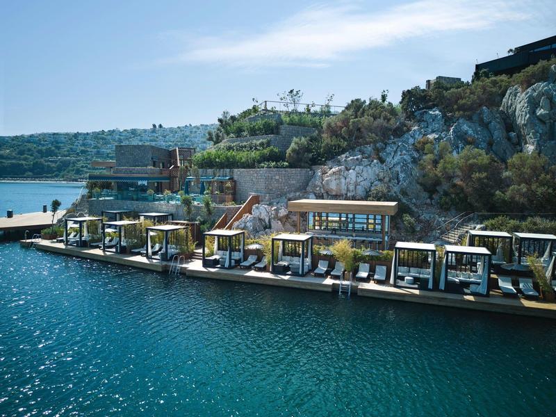 Salones flotantes con camas sobre agua clara junto a costa rocosa y casas